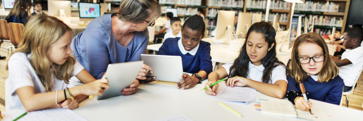 White older female teacher with mixed primary pupils around table