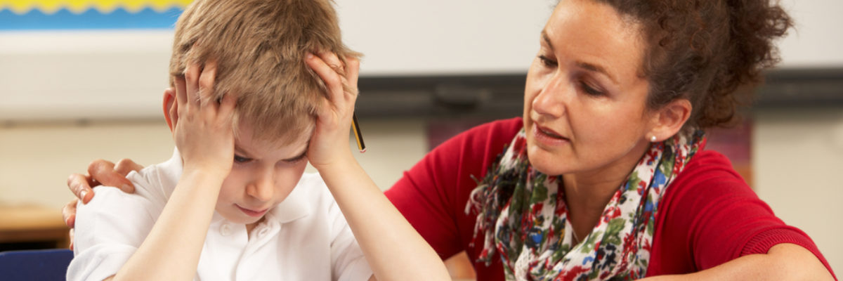 White stressed primary schoolboy with mixed race female teacher