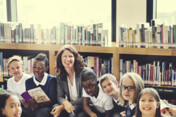 White female teacher and mixed primary pupils in library